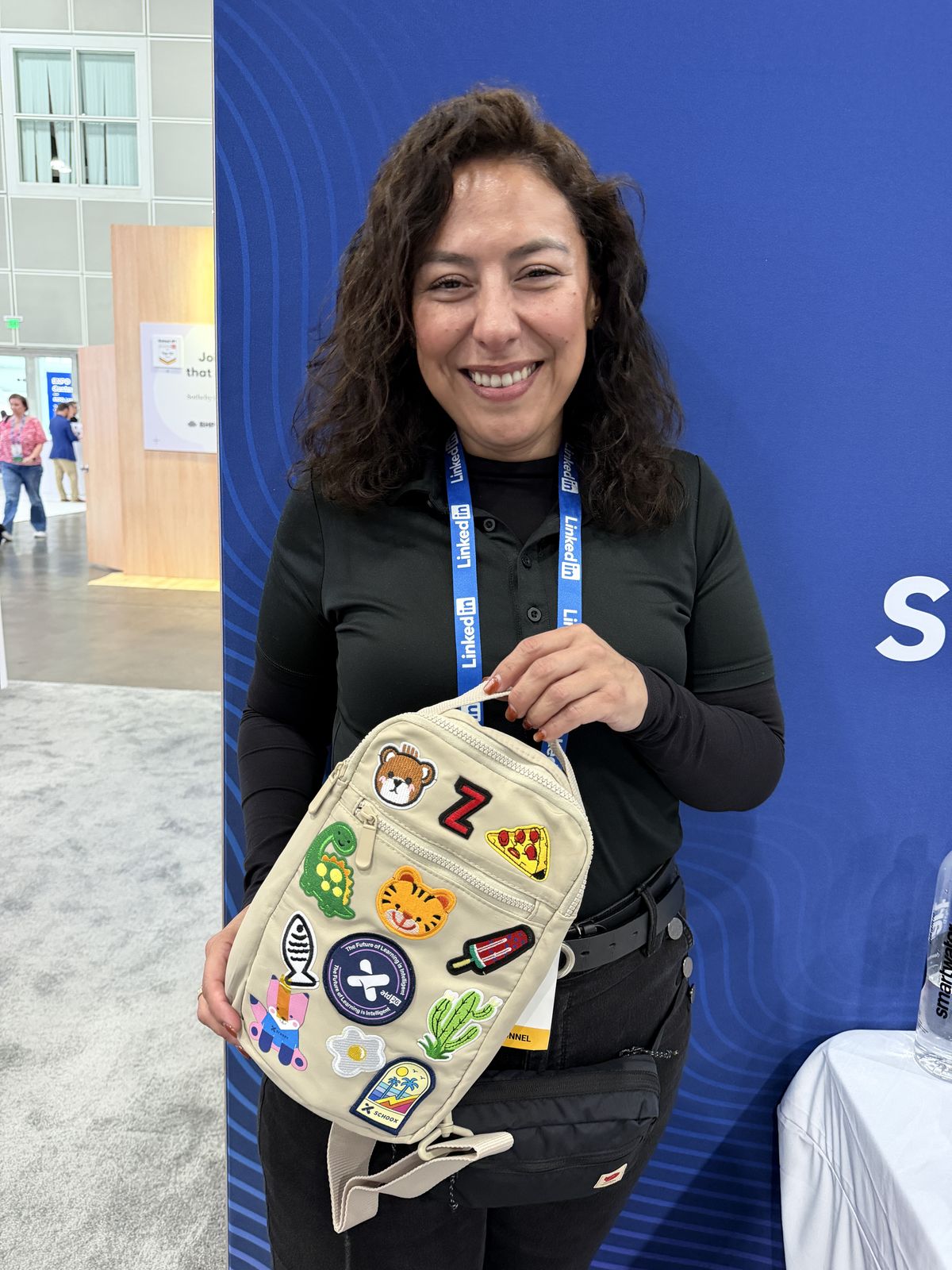 Attendee at a convention booth smiling and holding a bag decorated with embroidered animal and food patches